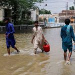 Men walk through rain waters, following rains and floods during