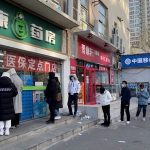 People wearing masks line up outside a pharmacy to buy