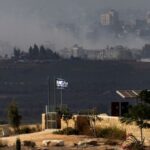 Israeli flag flies as smoke rises from Gaza in the