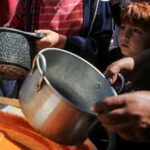Palestinians wait to receive food cooked by a charity kitchen,