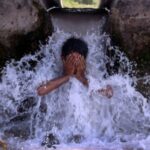 A boy cools off under a water pipe from a