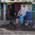 A woman sprays water in front of her roadside home