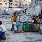 A Palestinian man and children push a cart with water