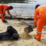Workers clean up the oil slick at Tanjong Beach in