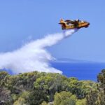 A firefighting plane drops water over an area affected by