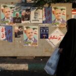 A woman walks near posters of presidential candidates Masoud Pezeshkian