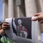 People handle a Vatican newspaper L’Osservatore Romano containing a photograph