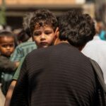 A migrant worker carries his son as he arrives at