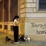 A woman walks with her dogs next to a graffiti