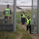 Police officers walk towards a newly erected security fence on