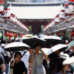 Visitors holding parasols walk along Nakamise street at the Asakusa