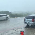 Vehicles stand on a road during a storm, in Green
