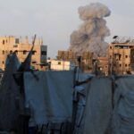 Palestinians stand as smoke rises following an Israeli strike, in