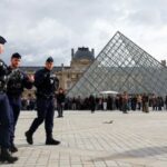French CRS riot police walk near the glass Pyramid of the Louvre