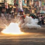 People run past a sound grenade fired by police to