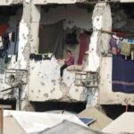 Displaced Palestinian girl sits on a wall of a damaged