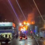 A person stands by an emergency vehicle as fire and