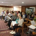 A conductor gestures during a choir rehearsal with patients ahead