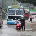 People and vehicles wade through a waterlogged street following heavy