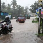 A man rides a motorbike along a waterlogged street following