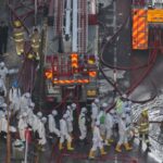 Police officers wearing protective suits walk near the site of