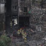Firefighters walk through charred bamboo scaffolding as they exit a
