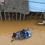 People ride in a boat at a flooded area, following