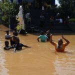 People wade through a flooded street, following Cyclone Ditwah in
