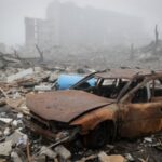 A destroyed car near apartment buildings damaged by Russian military