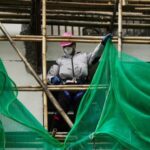 Worker removes scaffolding mesh from a building at Sui Wo