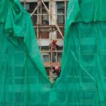 Workers remove scaffolding mesh from a building at Sui Wo