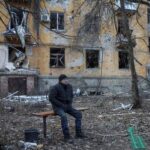 A resident sits near an apartment building damaged by Russian
