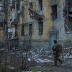 Ukrainian serviceman walks near an apartment building damaged by Russian