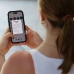 A teenager poses holding a mobile phone displaying a message