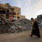 Palestinian woman walks past residential buildings damaged and destroyed during
