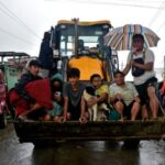 Flood-affected people sit in the scoop of a digger as