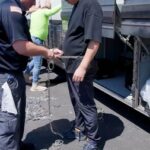 A detainee is handcuffed before boarding a bus, during a