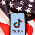 Tik Tok logo is displayed on the smartphone while standing