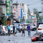 People clean mud from a street following flooding brought by