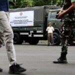 An Indonesian military officer stands beside a truck carrying multivitamins