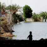 Children walking by their flooded homes in Dalhamo Village, at