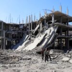 Palestinians walk past a destroyed building, as they inspect the
