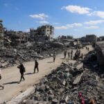 Palestinians walk past the rubble of destroyed buildings, amid a