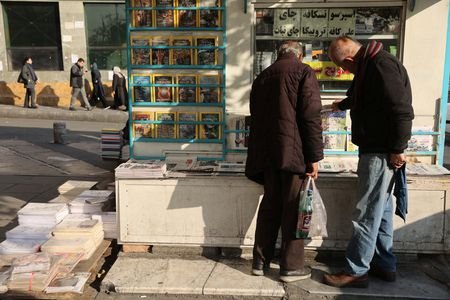 Iranian men read newspapers on a street, as protests erupt