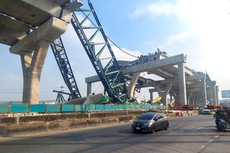 Cars drive next to a collapsed crane that crushed two