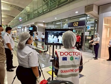 Airport health authorities wearing protective masks monitor passengers from international