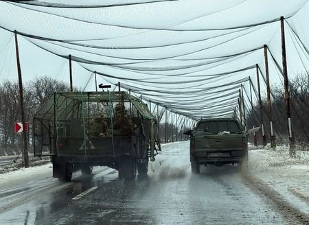 Ukrainian servicemen ride in a vehicle on a road covered