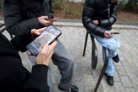 FILE PHOTO: Teenagers look at their mobile phone screens in
