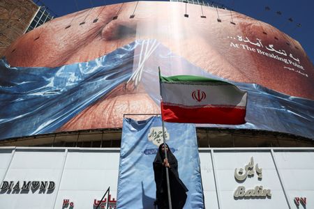 A woman holds an Iranian flag near an anti-U.S. billboard