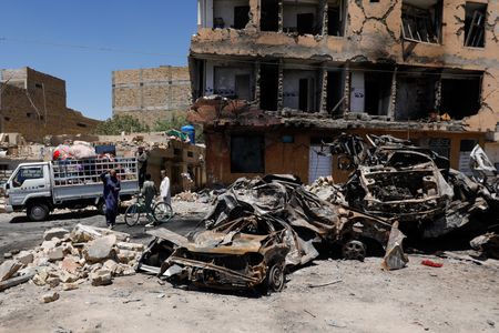 Residents stand next to a damaged building, rubble and destroyed